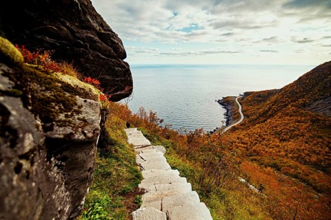 A stone path leads to a scenic view of the sea and a winding road down the hill, mountains, rocks,