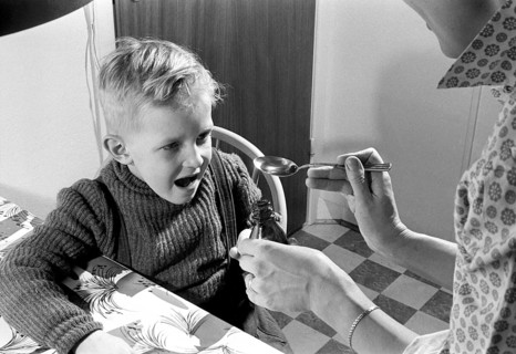 A boy is sick and won't take his medicine. His mother holds out a spoon and waits for him to gape
