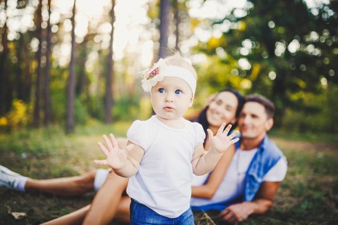Little girl one year on the background of parents resting on graß learning to walk on nature in the