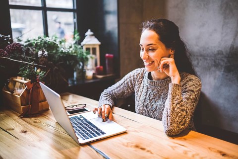 Beautiful young brunette woman using a laptop at coffee shop at a wooden table near window typing