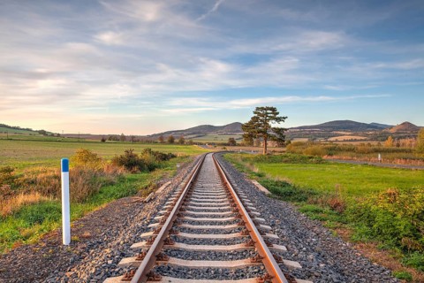 Old Railway tracks running through a field stretch to rural countryside at sunset. Single railway
