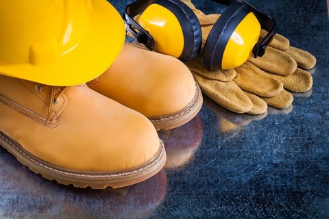 Waterproof boots leather protective gloves earmuffs and building helmet on scratched metallic