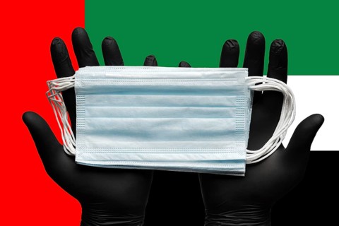 Doctor holds medical face mask in hands in black gloves on background colors national flag of