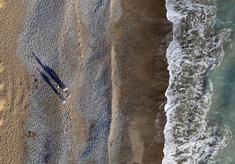 Aerial drone point of view of person walking on sand in a beach. Stormy waves idyllic beach in