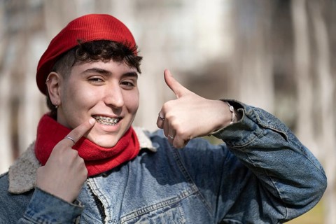 Young man smiling at the camera with thumb up showing his braces