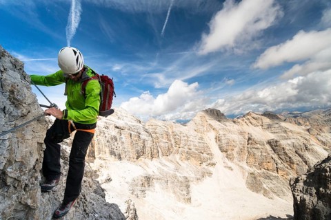 handsome male climber on a steep and exposed rock face climbs a Via Ferrata in Alta Badia in the