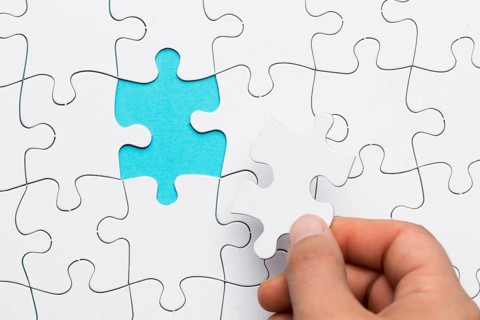 Human hand inserting white puzzle empty space