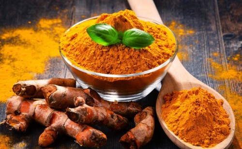 Composition with bowl of turmeric powder on wooden table