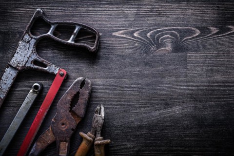 Rough vintage handsaw wire-cutter pliers on wooden board construction concept