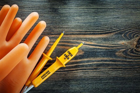Pair of insulating gloves Electrical tester on wooden board