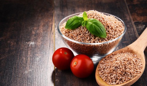 Bowl of uncooked spelt on wooden table