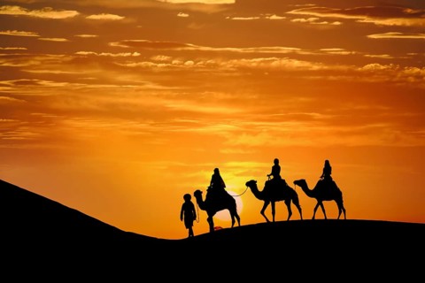 Three passengers and their handler travel in the Saharan Desert in Morocco
