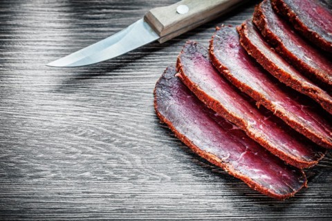 Smoked meat cut into slices, knife on wooden board