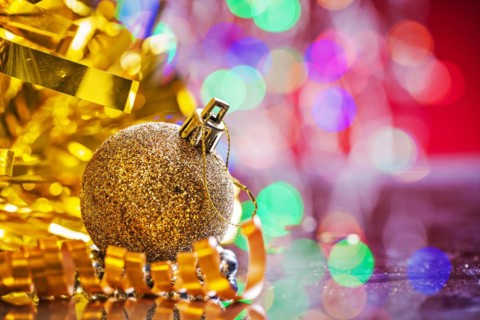 Gold colored christmas ball with tinsel and tape on mirror surface and blurred background