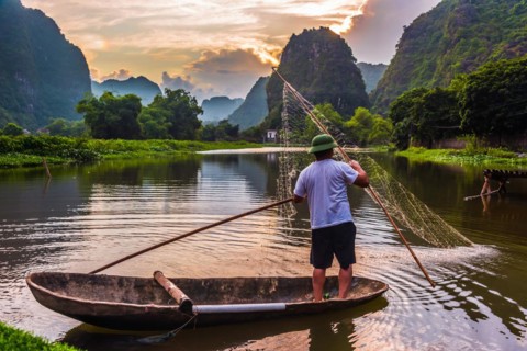 Fisherman on boat in Trang An, a scenic area near Ninh Binh, Vietnam inscribed as a UNESCO World