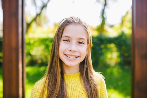 Portrait of modern happy teen girl with braces dressed in yellow clothes in park. Pretty teenage