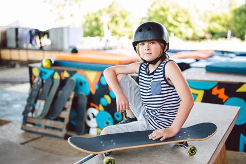 Boy sitting at skatepark, looking camera. Kid resting with skate board at skate park. child sits on