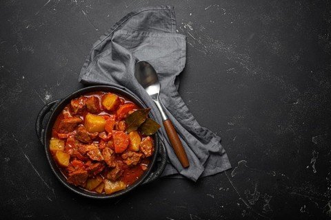 Beef meat stew with potatoes, carrot and delicious gravy in black casserole pot with bay leaves