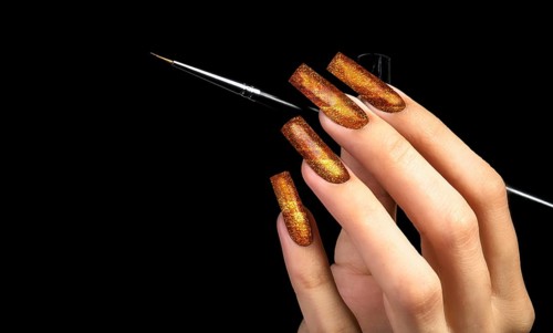 Hand with a beautiful golden manicure and a brush on a black background. Nail design. Extended