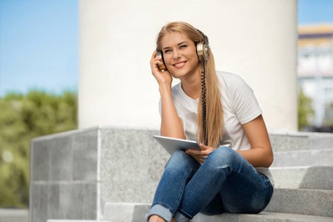 Happy young woman listening to music with vintage headphones, surfing the internet on a tablet PC