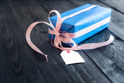 Classy blue gift, tied with pink ribbon and bow, with an empty label tied to it, on an old wooden