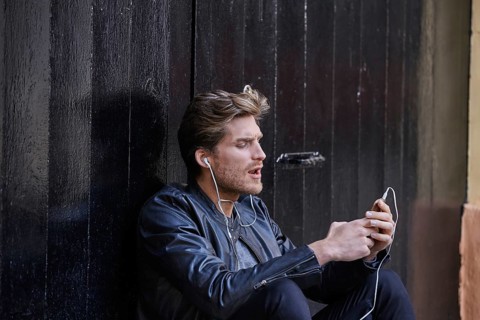 Young man listening music with smartphone earphones sitting in the street black door