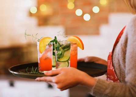 Young pretty woman with red and green cocktails on tray in the bar
