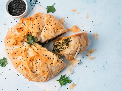 Greek pie spanakopita on white baking paper over blue background. Ideas and recipes for vegetarian