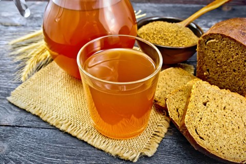 Kvass in glassful and glass jug on burlap, malt in a bowl, rye bread and ears on a wooden plank