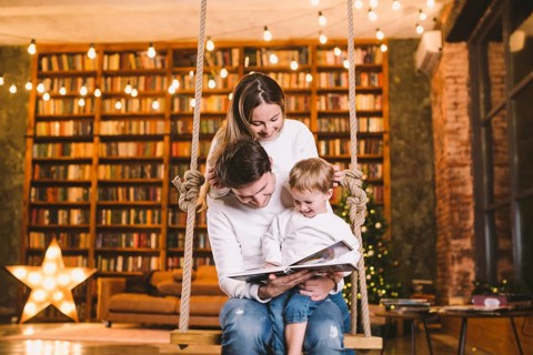 Family with baby relaxing at home swing seat in cosy dark living room on Christmas eve. Family