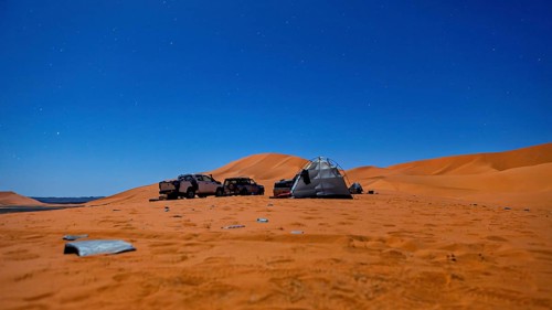 Camping scene in the desert under a starry night sky with tents and vehicles, tent camp in the
