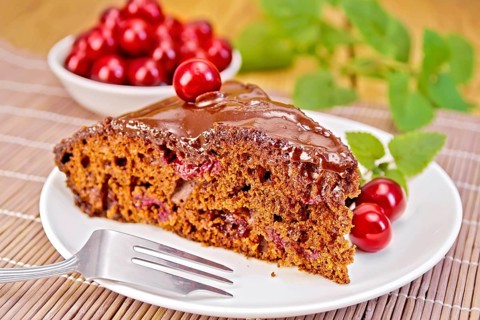 Chocolate cake with cherries on a plate, cherries, mint on a bamboo napkin on the background of