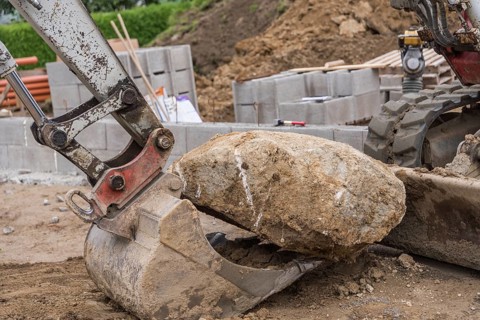Excavator shovels large stone onto shovel - Construction industry, Construction site