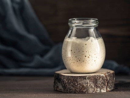 Active wheat sourdough starter in glass jar on brown wooden background. Starter for sourdough bread