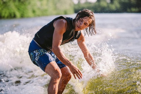 Active wakesurfer jumping on wake board down the river waves. Surfer on wave. Male athlete training