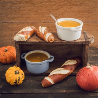 Homemade pumpkin soup in little cocotte cups and pretzel sticks on wooden table