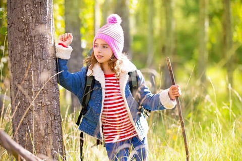 Hiking kid girl with backpack in autum poplar trees forest and walking stick