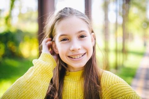 Beautiful and happy teenage girl with braces smiling to camera in yellow clothes in park. Concept