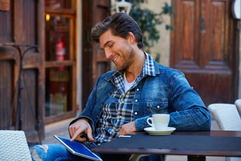 Young man with tablet pc touch in an cafe outdoor having some coffe cup