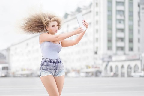 Happy young woman with vintage music headphones around neck taking selfie with tablet PC and