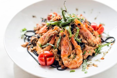 Gourmet food grilled prawn and vegetables on black squid ink pasta meal