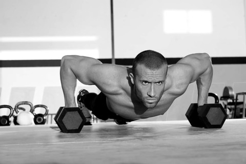 Gym man push-up strength pushup exercise with dumbbell in a crossfit workout