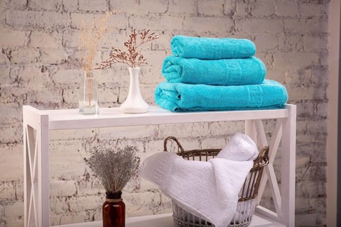 Rack with a stack of three colour turquoise towels and baskets with clean white towels and toilet