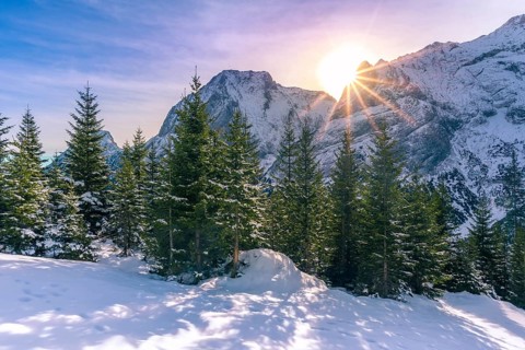Serene winter landscape with a bright sun shining over the peaks of the Austrian Alps and its