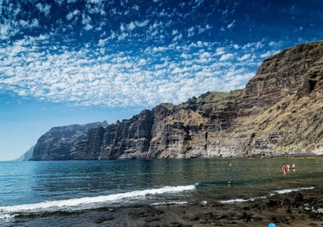 Tourists bathing at los gigantes volcanic black sand beach by famous natural cliffs landmark in