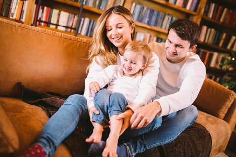 Christmas family portrait. Young Caucasian family in identical clothes having fun on sofa in living