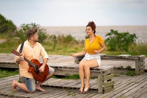 Woman dancing sitting on a beach while her boyfriend plays the guitar
