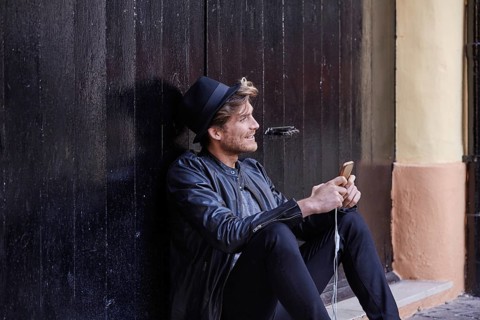 Young man with smartphone earphones sitting in the street black door