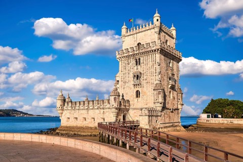 Belem tower and wooden bridge to it, Lisbon, Portugal at blue summer day sky with clouds. Medieval