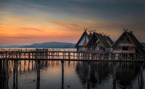 Weathered wooden cabins built on wooden pillars over the Bodensee lake water, at colorful sunset,